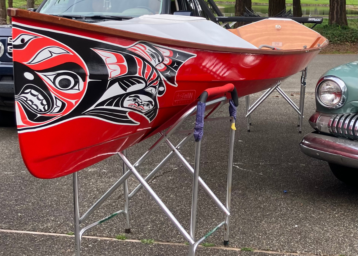 A red canoe with intricate indigenous art designs rests on metal stands outdoors.